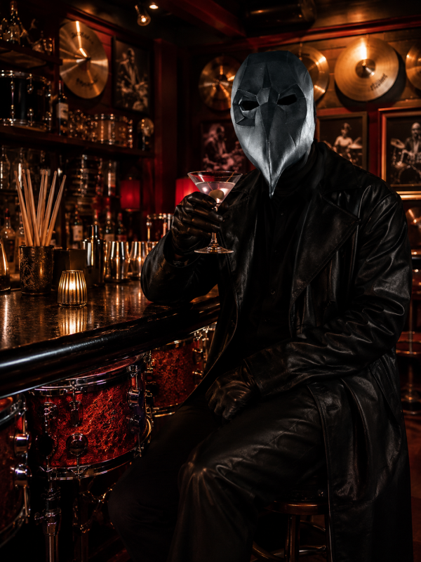 A masked figure in a black leather coat sits at a bar, raising a martini in a dim, club-like setting.