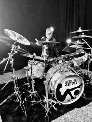 Masked drummer seated behind a glittery drum kit, logo reads Digital Zero, in a studio setting.
